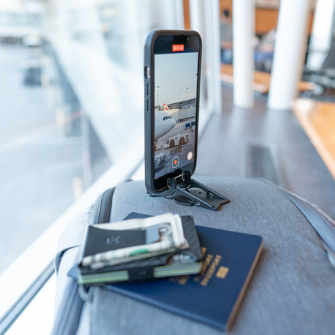 An iPhone on a Pocket Tripod taking a video of at an airport next to a wallet and a passport