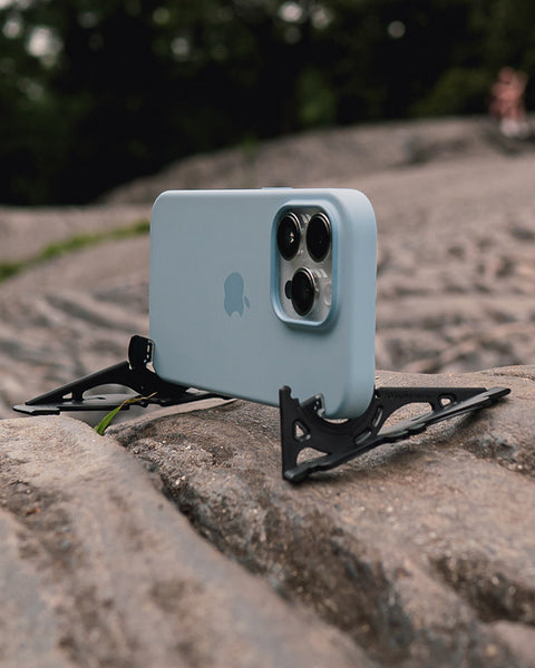 An iPhone in a slim case in horizontal orientation on an uneven rocky surface.