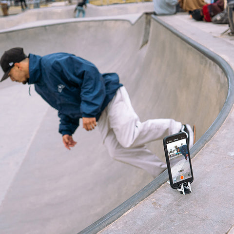 A phone on a Pocket Tripod above ramp capturing a skateboarder at Venice Beach doing a trick below it. 
