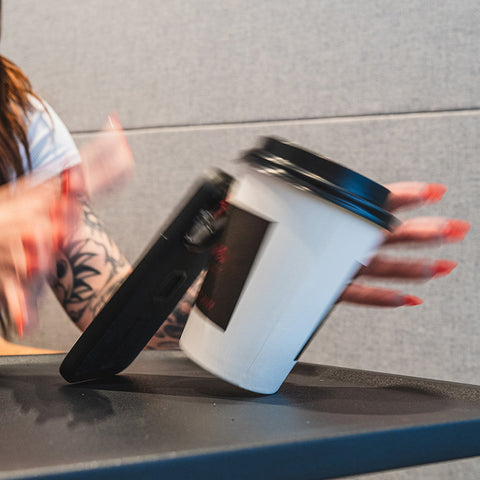 A phone being leaned against a cup of coffee and spilling the coffee.