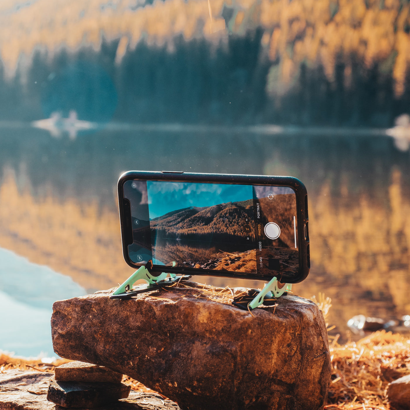A tripod holding a phone horizontally while taking a picture of a landscape on a rock