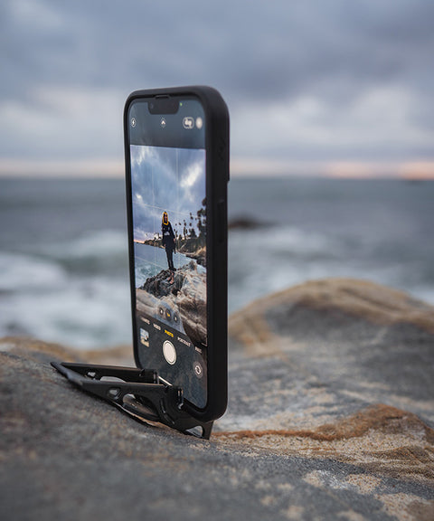 An iPhone being used with a Pocket Tripod to balance the phone on an uneven rocky surface to a take a solo photo by the water.
