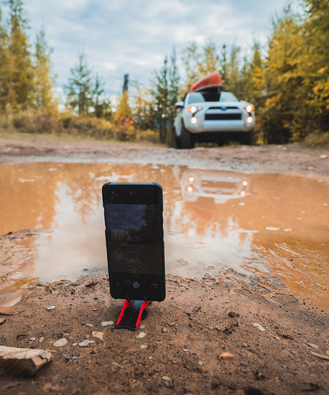 An android phone on a Pocket Tripod in the mud, protecting the phone's ports from dirt and grime