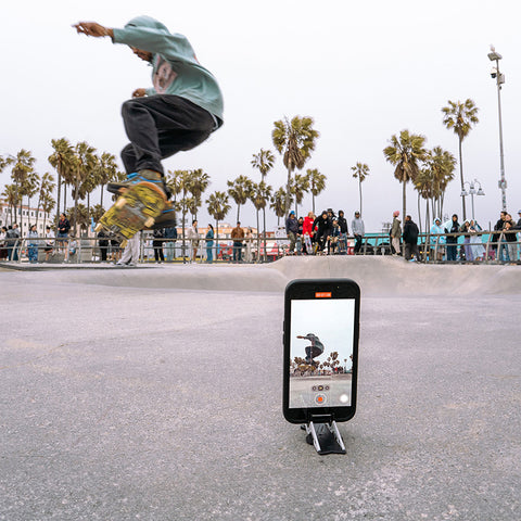 A phone on a Pocket Tripod capturing a skateboarder doing a trick in the air at Venice Beach