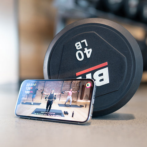 An iPhone leaned against a dumbbell weight with a workout video playing.